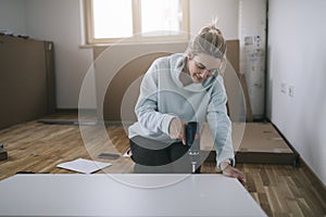 Woman using cordless screwdriver for assembling furniture