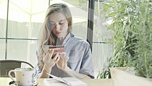 Woman using credit card for shopping online with smartphone in cafe.