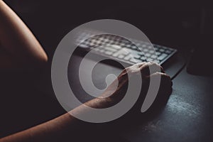 Woman using desktop computer mouse in dark home office interior, closeup of hands