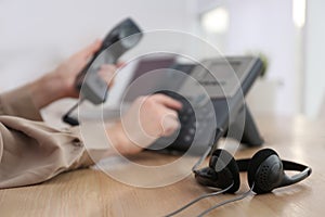 Woman using desktop telephone in office, focus on headset. Hotline service