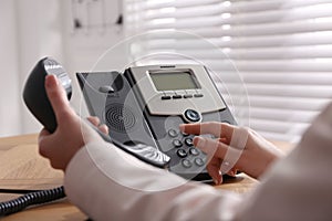 Woman using desktop telephone at wooden table in office, closeup. Hotline service