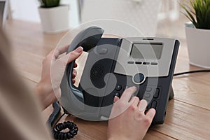 Woman using desktop telephone at wooden table in office, closeup. Hotline service