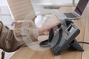 Woman using desktop telephone at wooden table in office, closeup. Hotline service