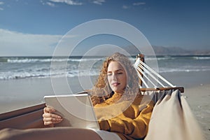 Woman using digital tablet while lying on hammock at beach