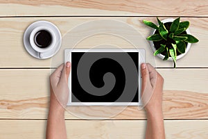 Woman using digital tablet PC against wooden table with cup of cofee and flower with copy space. Top view digital tablet lying on