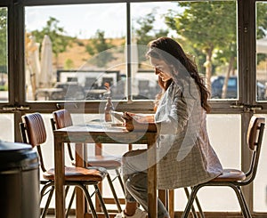 Woman using a digital tablet while sitting in a coffee shop next to the window