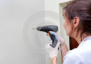 Woman using a drill drills a hole in the wall