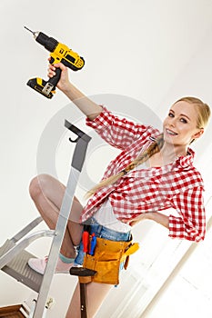 Woman using drill on ladder