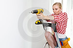 Woman using drill on ladder