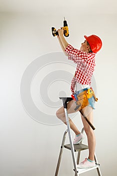 Woman using drill on ladder