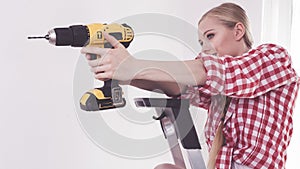 Woman using drill on ladder