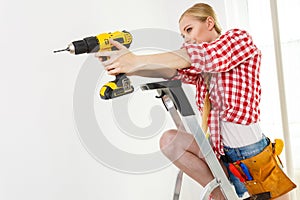 Woman using drill on ladder