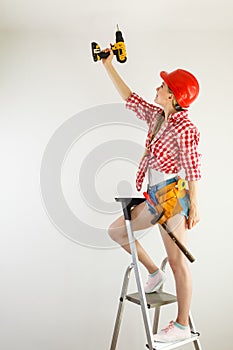 Woman using drill on ladder
