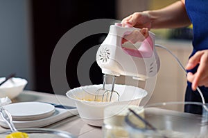 Woman using electric mixer to mix ingredients for dough while making cookies in the kitchen at home