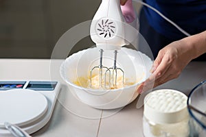 Woman using electric mixer to mix ingredients for dough while making cookies in the kitchen at home