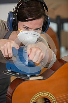 woman using electric sander on guitar for repairing