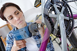 woman using electric screwdriver to repair bicycle gars