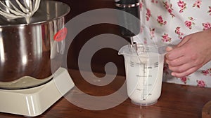 Woman is using a electric whisk for mixing cream in cup, on kitchen table