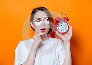Woman using eye patch for her eyes and holding alarm clock