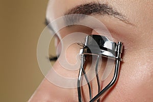 Woman using eyelash curler on beige background, closeup. Space for text