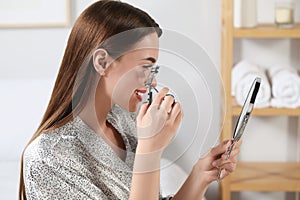 Woman using eyelash curler near mirror at home