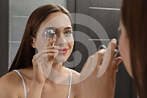 Woman using eyelash curler near mirror indoors