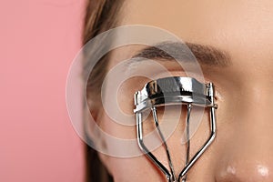 Woman using eyelash curler on pink background, closeup. Space for text