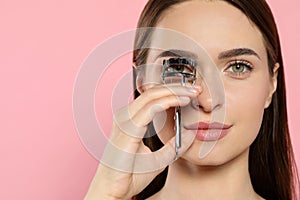 Woman using eyelash curler on pink background, space for text