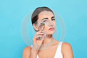 Woman using eyelash curler on turquoise background