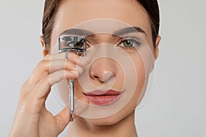 Woman using eyelash curler on white background, closeup