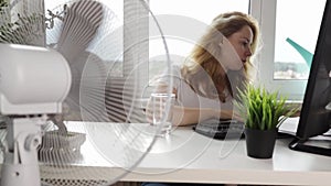 Woman using a fan to circulate air in the office during the summer, summer heat indoors