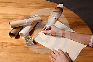 Woman using feather pen to write with ink on parchment at wooden table