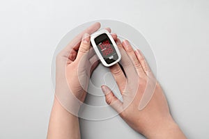 Woman using fingertip pulse oximeter on background, top view