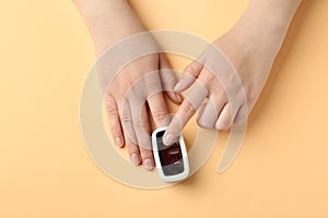 Woman using fingertip pulse oximeter on orange background, top view