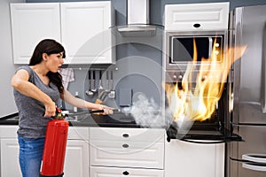 Woman Using Fire Extinguisher To Put Out Fire From Oven