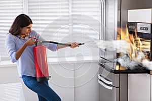 Woman Using Fire Extinguisher To Put Out Fire From Oven photo
