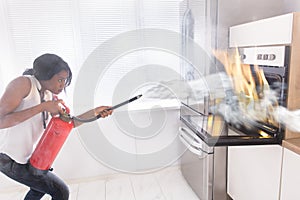 Woman Using Fire Extinguisher To Stop Fire Coming From Oven