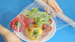 Woman using food film for food storage on a white table. Roll of transparent polyethylene food film for packing products