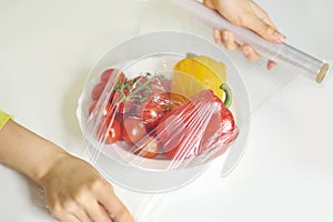 Woman using food film for food storage on a white table. Roll of transparent polyethylene food film for packing products