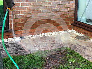 Woman using the garden hose to clean slabs in her back garden.