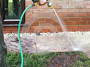 Woman using the garden hose to clean slabs in her back garden.