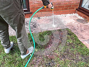 Woman using the garden hose to clean slabs in her back garden.