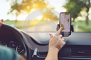 Woman using GPS navigation in mobile phone while driving car at sunset