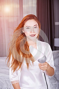 Woman using hair dryer in bedroom with soft light