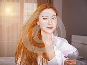 Woman using hair dryer in bedroom with soft light