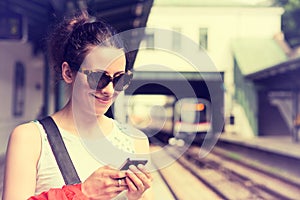 Woman using her cell phone on subway platform, checking train schedule