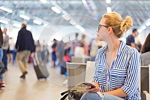 Woman using her cell phone while waiting to board a plane at departure gates at international airport.