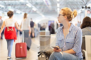 Woman using her cell phone while waiting to board a plane at departure gates at international airport.