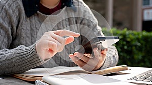 A woman using her smartphone, checking messages while working remotely at a table outdoors