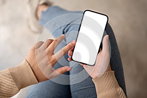 Woman using her smartphone while sitting indoors. A white-screen smartphone mockup. touching screen